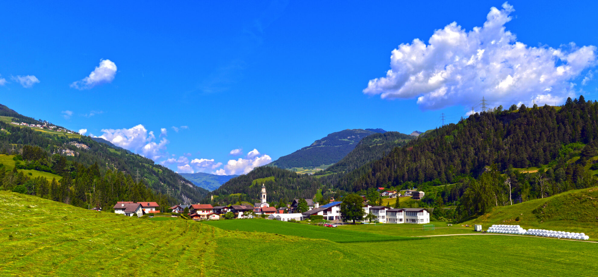 Idyllisches Bergdorf in den Alpen – grüne Wiesen, Wälder und Panorama-Blick auf die Berge.