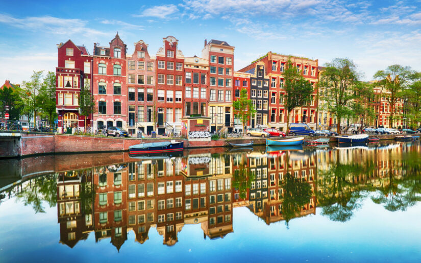 Bunte Grachtenhäuser in Amsterdam mit Spiegelung im Wasser – Niederlande erleben