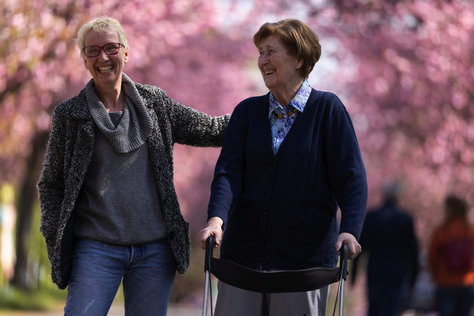 Zwei Frauen genießen den Frühling beim Spaziergang – Reisen mit Rollator ermöglichen unbeschwerte Momente, Gemeinschaft und barrierearmes Reiseerlebnis mit dem Reisering Hamburg.