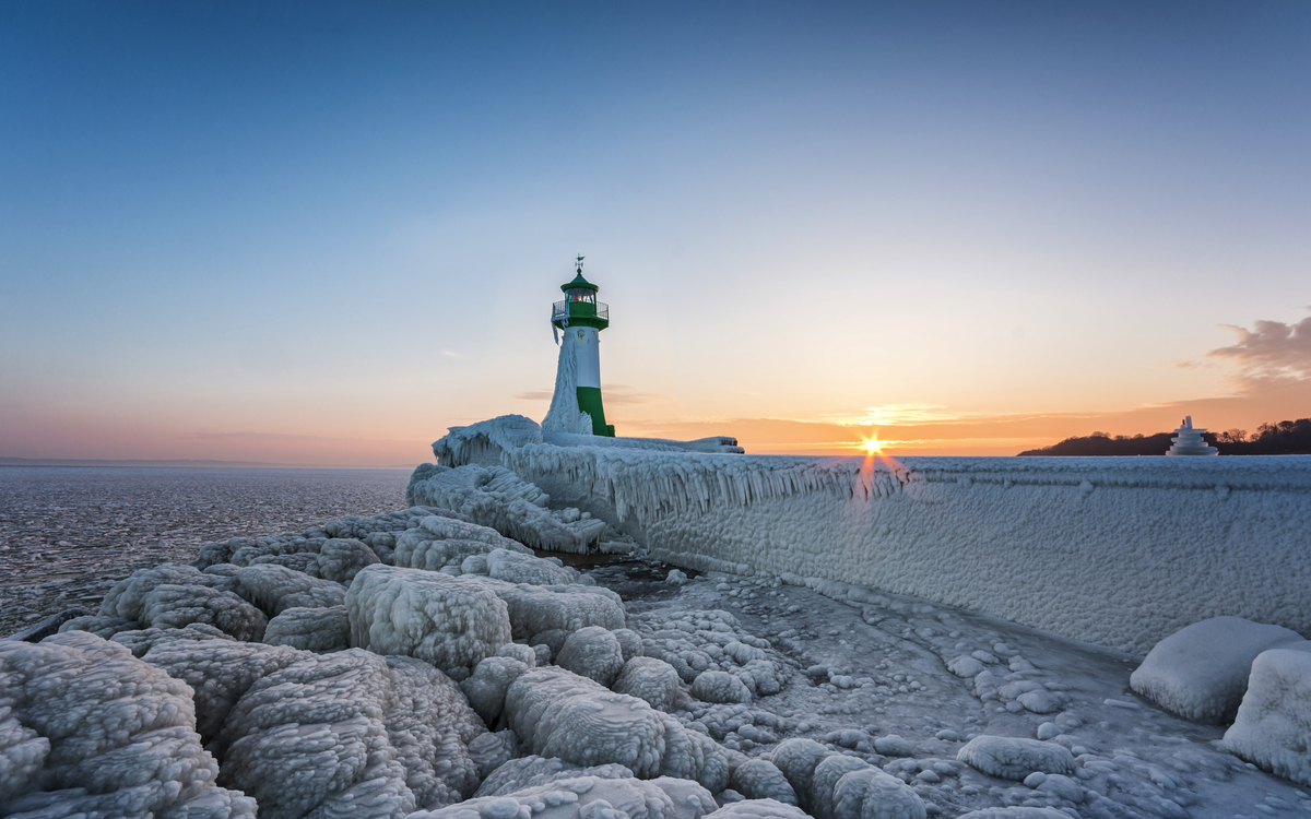 Vereister Leuchtturm bei Sonnenuntergang am Meer.