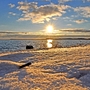 Verschneite Küste bei Sonnenuntergang mit Blick auf das Meer.