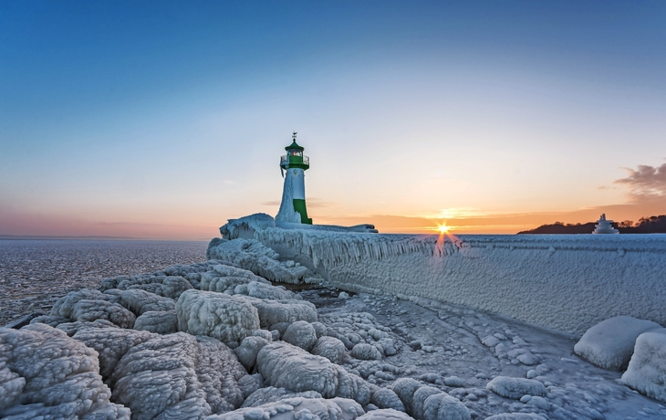 Vereister Leuchtturm bei Sonnenuntergang am Meereshorizont.