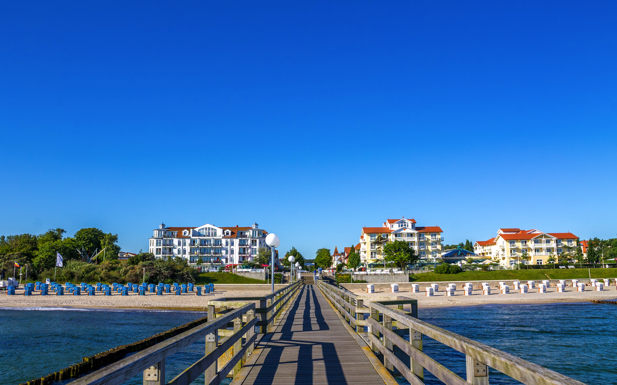 Steg mit Ausblick auf Strand, Bäume und Gebäude bei klarem Himmel.