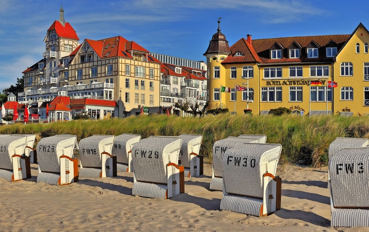 Strandkörbe am Sandstrand vor historischen Gebäuden bei sonnigem Wetter.