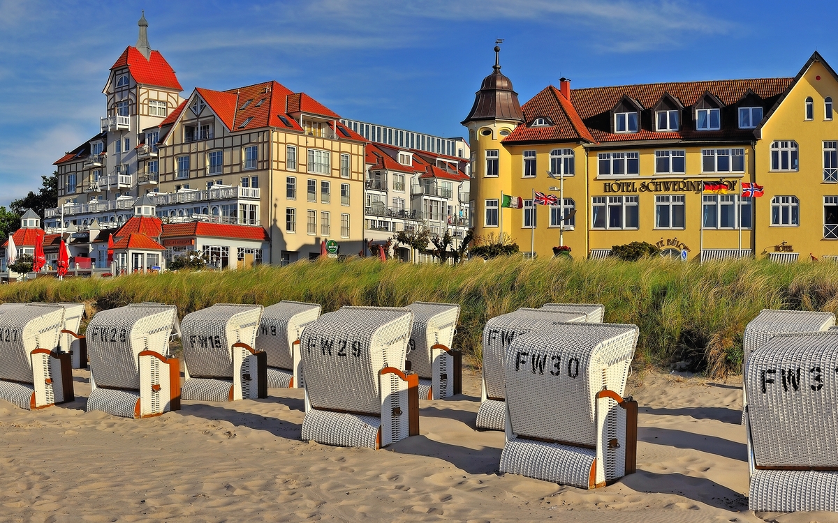 Strandkörbe am Sandstrand vor historischen Gebäuden bei sonnigem Wetter.