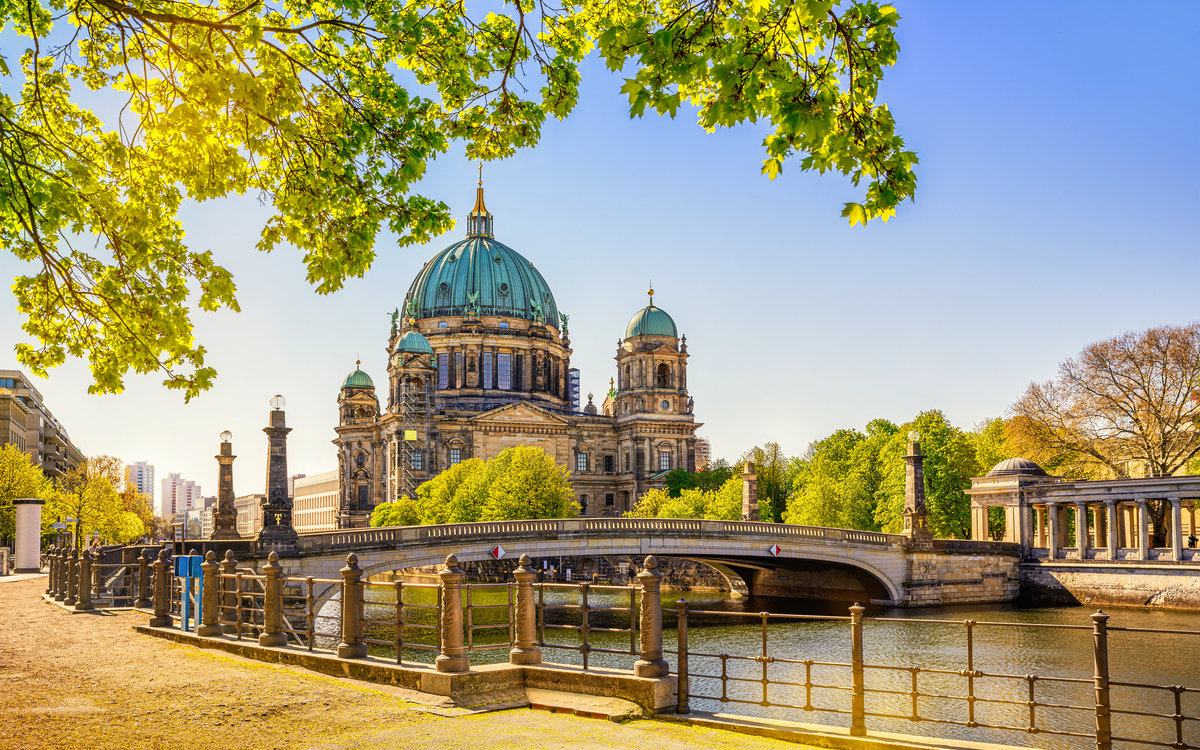 Berliner Dom im Sommer bei sonnigem Wetter, an der Spree gelegen, umgeben von grünen Bäumen.