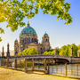 Berliner Dom im Sommer bei sonnigem Wetter, an der Spree gelegen, umgeben von grünen Bäumen.