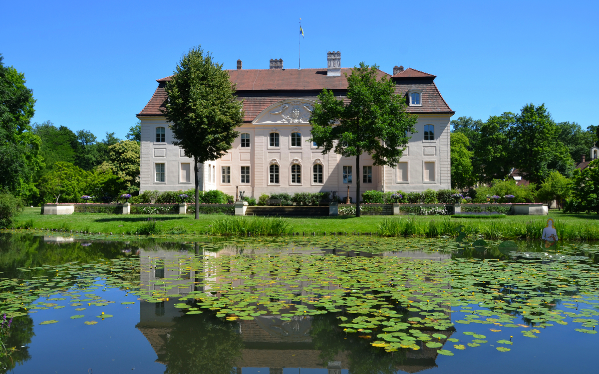 Herrenhaus mit Spiegelung in einem Teich voller Seerosen, sonniges Wetter.