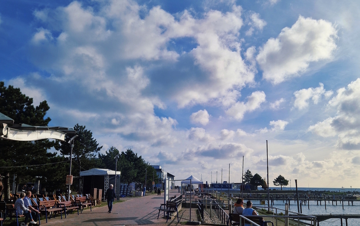 Promenade mit Sitzbänken und Wolken am Strand von Damp.