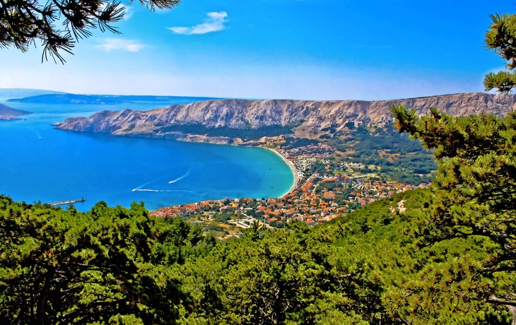Küstenlandschaft mit blauem Meer und grüner Vegetation im Vordergrund.