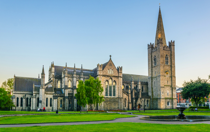 Historische Kathedrale mit grünem Park und blauem Himmel im Hintergrund.