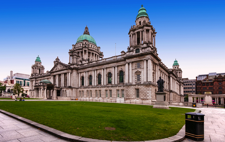 Großes, historisches Gebäude mit Kuppeln und Statuen, umgeben von Grünfläche.