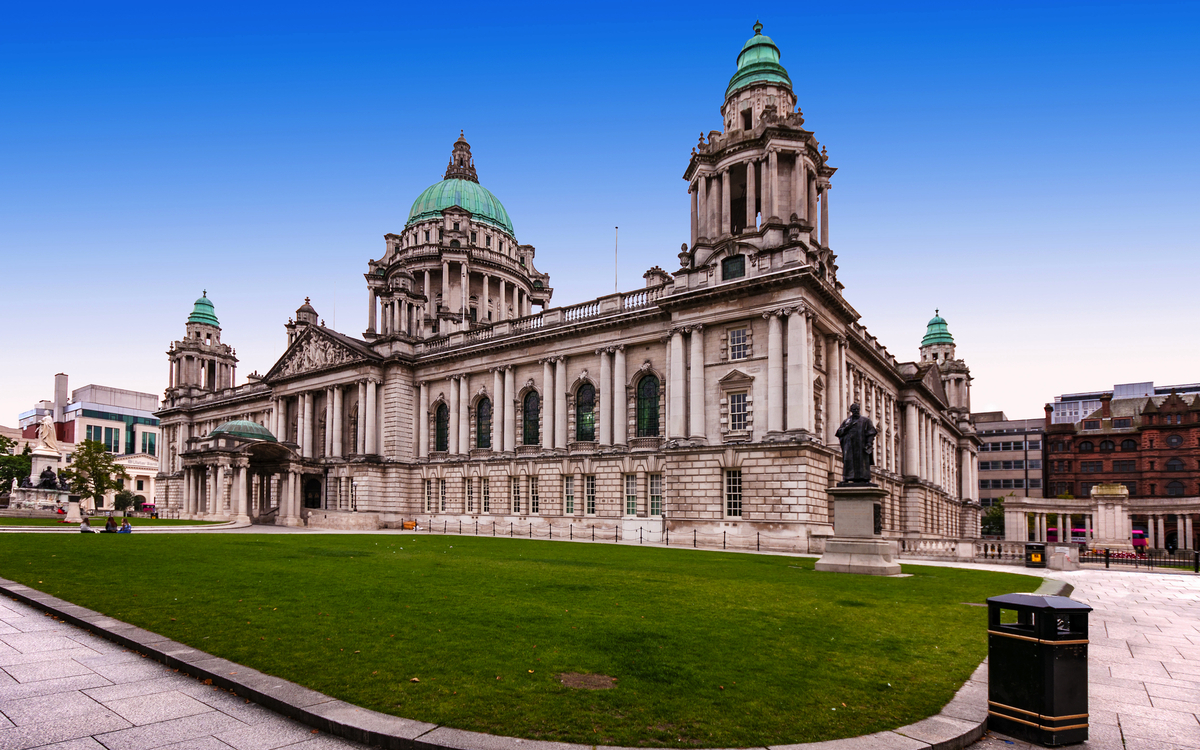Großes, historisches Gebäude mit Kuppeln und Statuen, umgeben von Grünfläche.