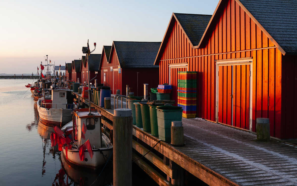 Rote Bootshäuser und Fischkutter entlang eines Holzdocks in der Abenddämmerung.