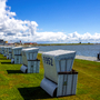 Strandkörbe auf einer Wiese am Meer, blauer Himmel mit Wolken.