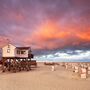 Haus auf Stelzen am Strand bei Sonnenuntergang mit Wolken und Strandkörben.