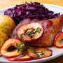 Gebackene Entenkeule mit Rotkohl, Klößen und Apfelscheiben auf einem weißen Teller.