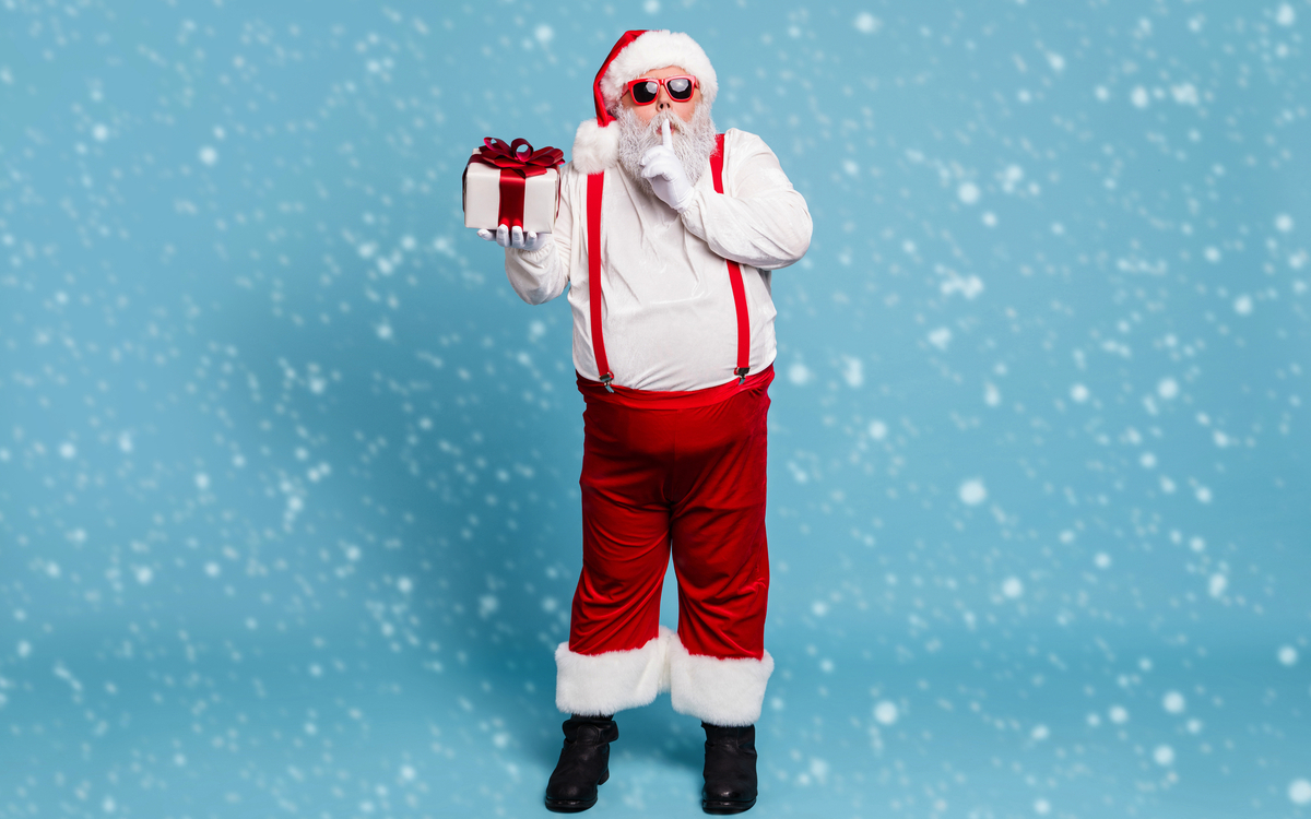 Weihnachtsmann mit Geschenken vor blauem Hintergrund mit Schneefall.