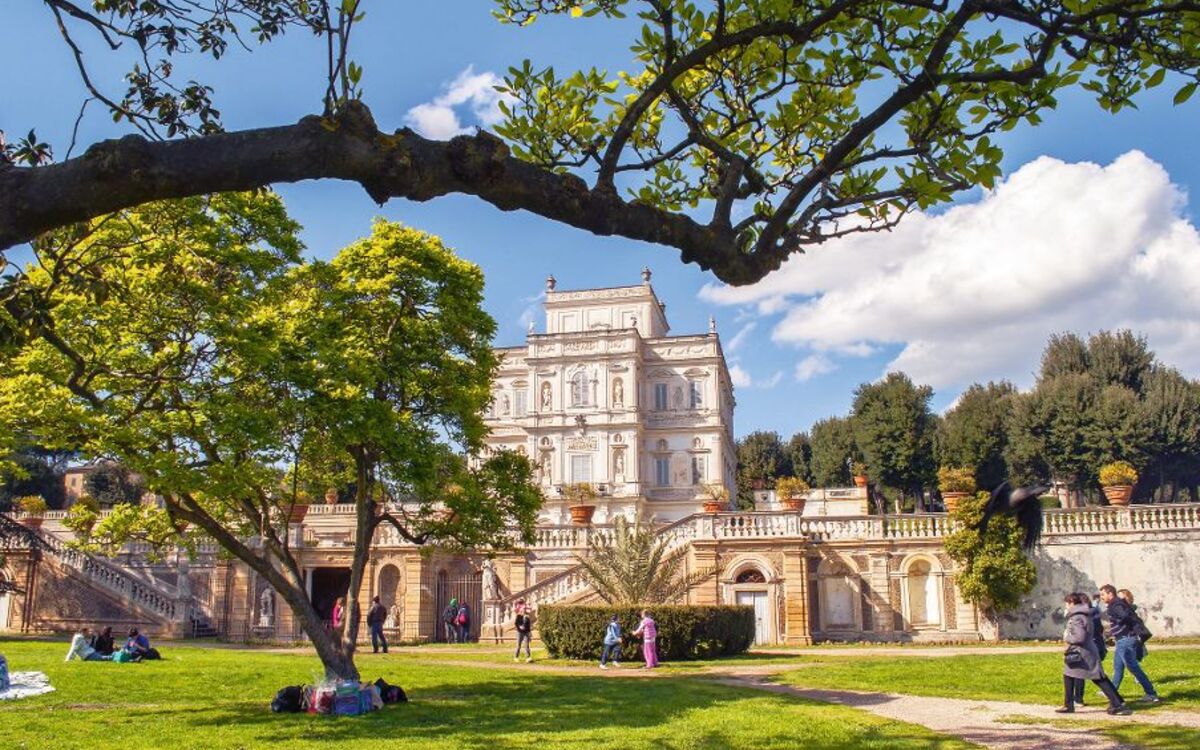 Villa Doria Pamphili Großer historischer Palast mit Garten und Bäumen, Menschen spazieren auf dem Rasen.