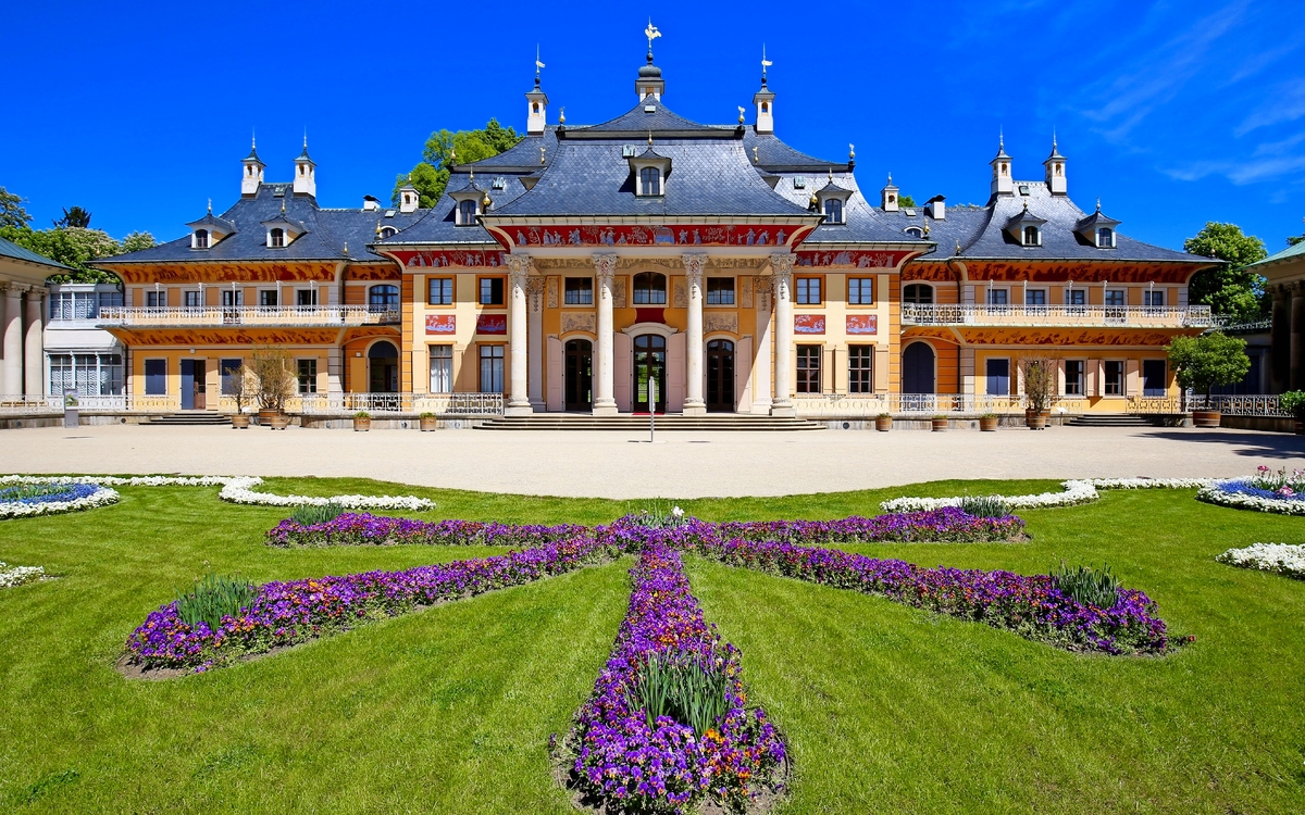 Pillnitz Barockschloss mit Garten und blühenden Blumen im Vordergrund.