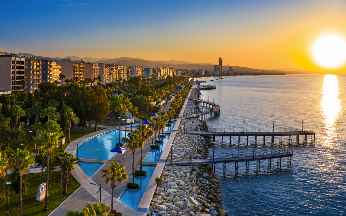 Küstenpromenade bei Sonnenuntergang mit Meerblick und Palmen.