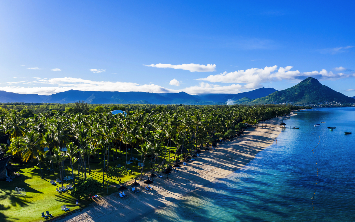Strand mit Palmen, klarem Wasser und Bergen im Hintergrund bei sonnigem Wetter.