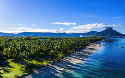 Strand mit Palmen, klarem Wasser und Bergen im Hintergrund bei sonnigem Wetter.