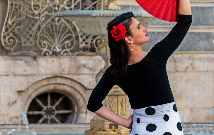 Frau in Flamenco-Kleidung mit rotem Fächer vor Brunnen.
