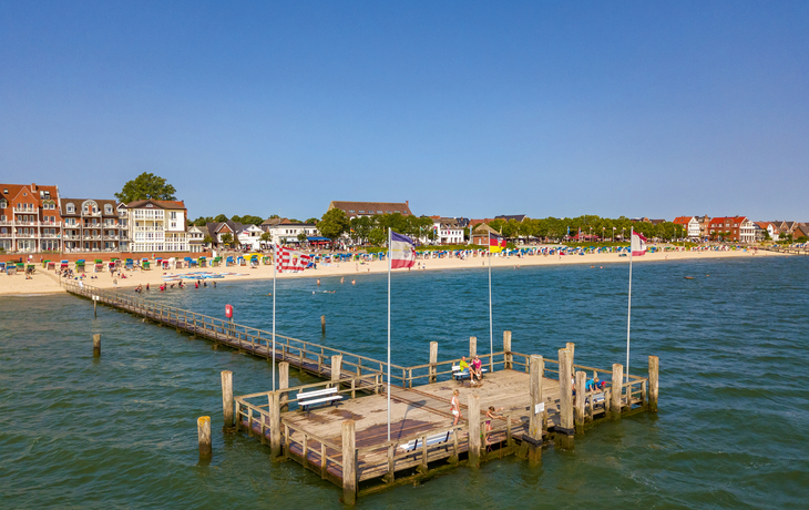 Steg am Meer mit Blick auf Strand und Gebäude im Hintergrund bei klarem Himmel.