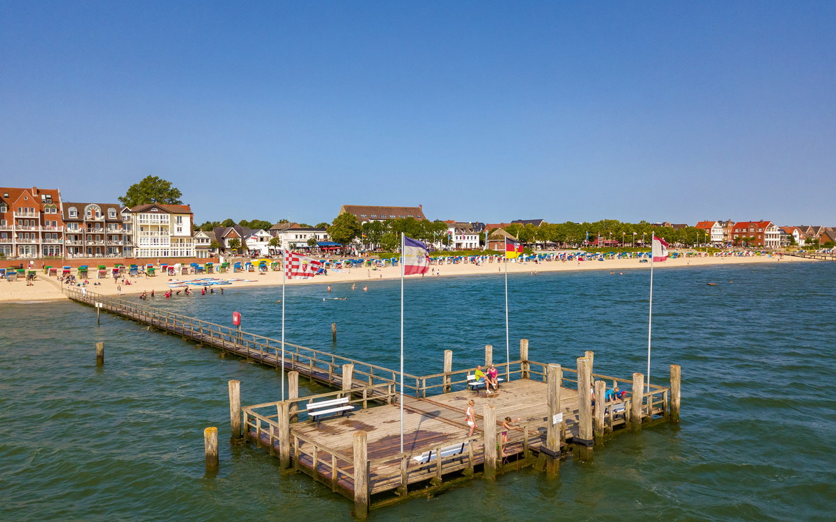 Steg am Meer mit Blick auf Strand und Gebäude im Hintergrund bei klarem Himmel.