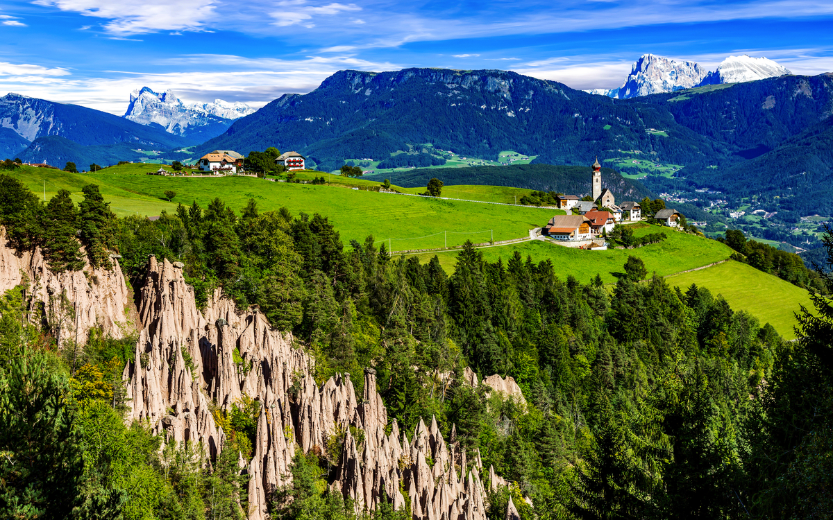 Malerische Landschaft mit Bergformationen und einem Dorf im Hintergrund.