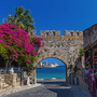 Stadttor mit Bougainvillea, Meerblick und Souvenirladen im Vordergrund.