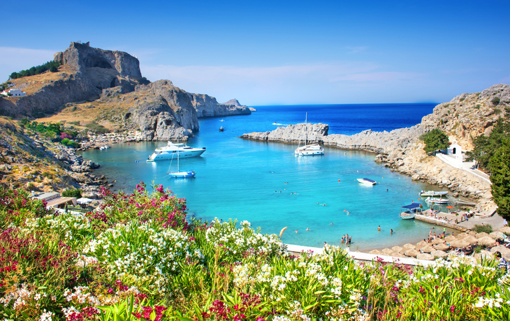 Malerische Bucht mit blauem Wasser, Segelbooten und grünen Hügeln im Hintergrund.
