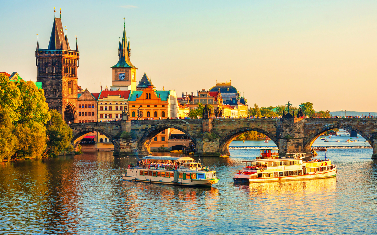 Boote auf einem Fluss vor einer alten Steinbrücke in einer Stadt bei Sonnenuntergang.