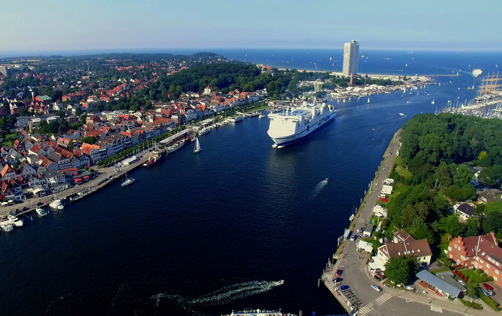 Luftaufnahme eines Hafens mit einem großen Kreuzfahrtschiff und Küstenstadt im Hintergrund