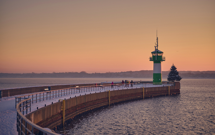 Leuchtturm bei Sonnenuntergang an einem schneebedeckten Steg.