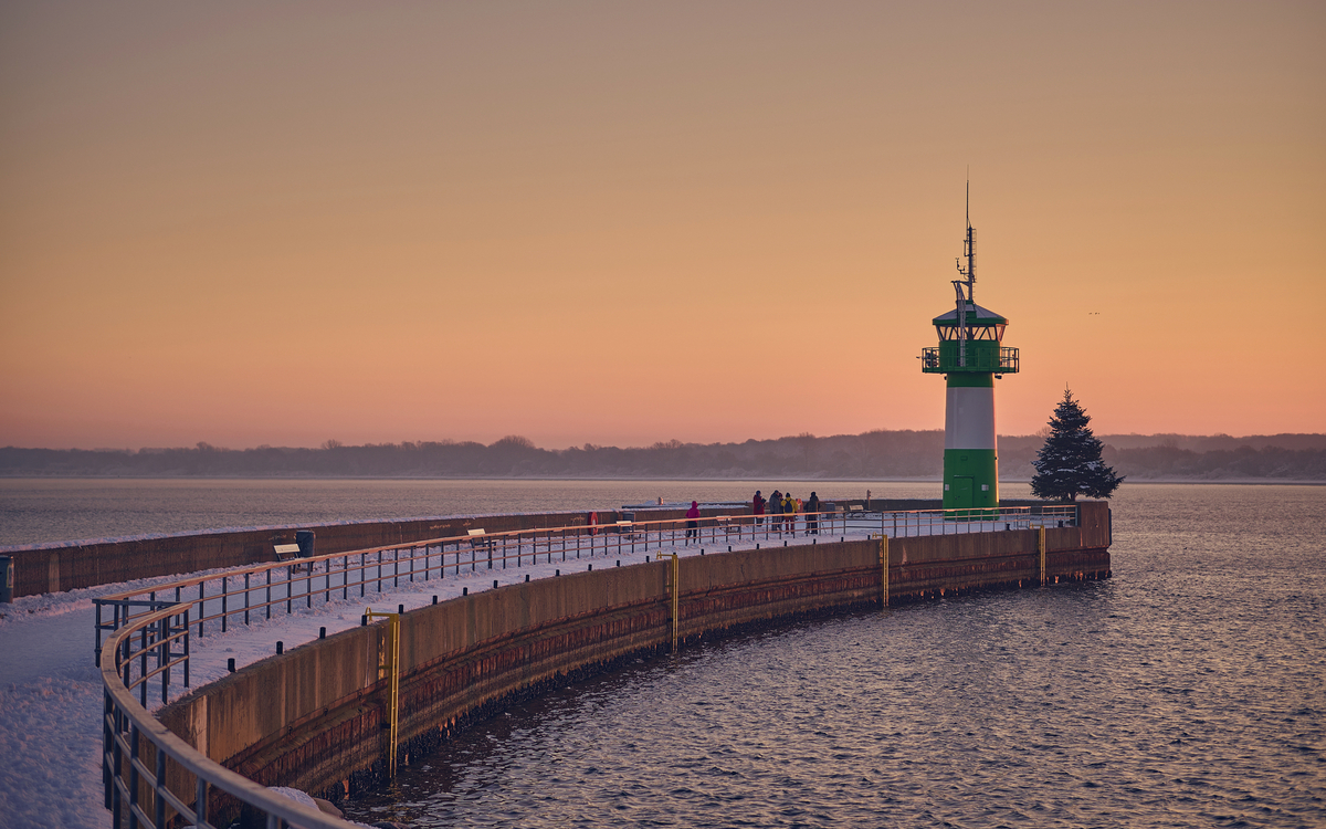 Leuchtturm bei Sonnenuntergang an einem schneebedeckten Steg.