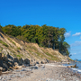 Klippenküste mit Bäumen und steiniger Strand bei blauem Himmel.
