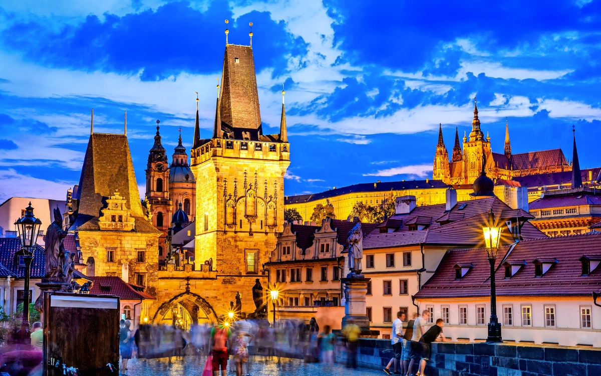 Karlsbrücke in Prag bei Sonnenuntergang mit Menschen und blauem Himmel.