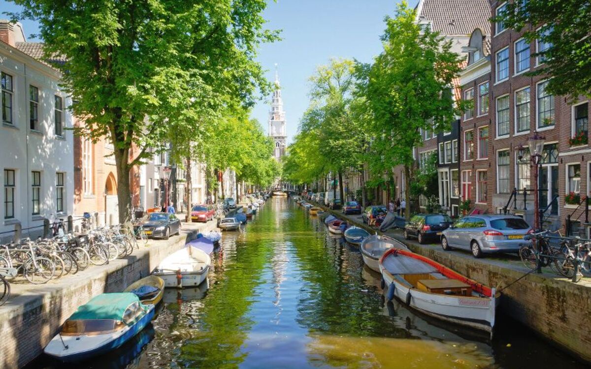 Blick auf eine typische Amsterdamer Gracht mit Booten, gesäumt von Bäumen und traditionellen niederländischen Gebäuden.