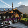 Traditionelles Holzhaus mit Blumen vor Bergkulisse bei Sonnenschein.