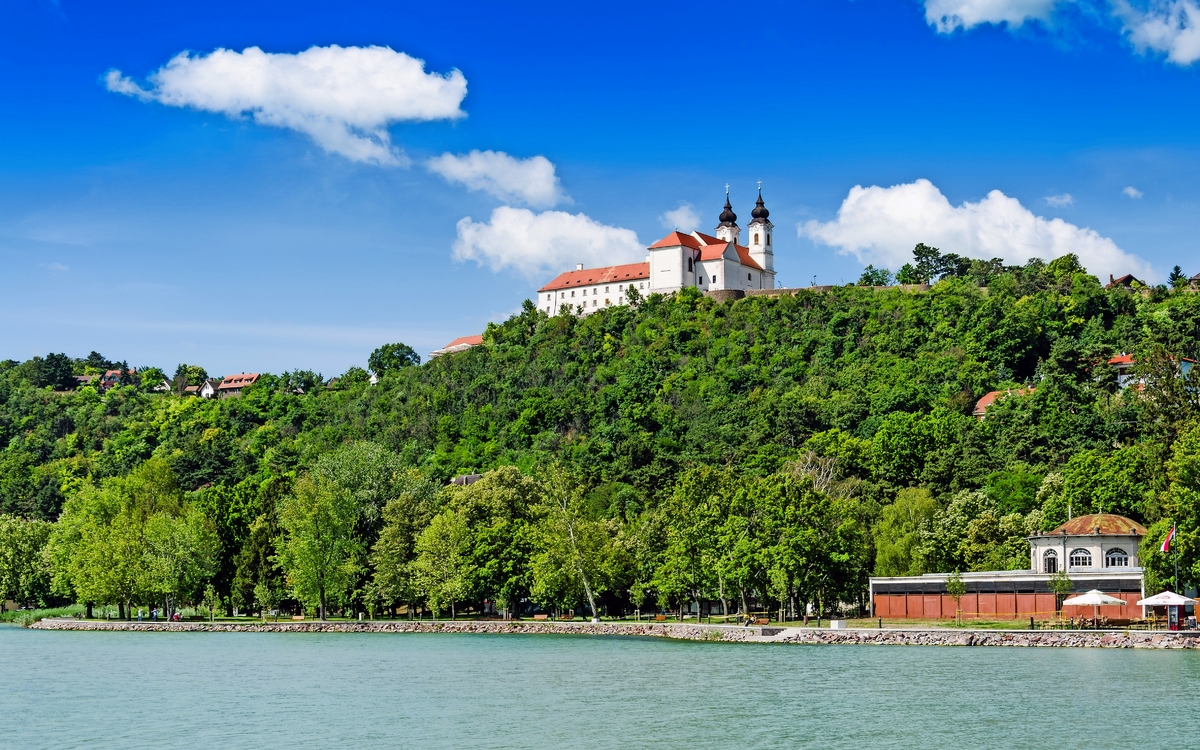 Kloster auf einem Hügel mit Bäumen und blauem Himmel im Hintergrund.