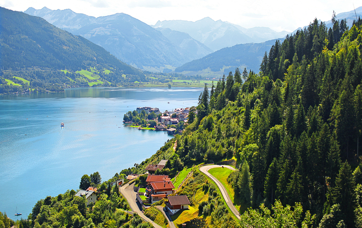 Blick auf einen See in den Alpen, umgeben von Wäldern und Bergen.