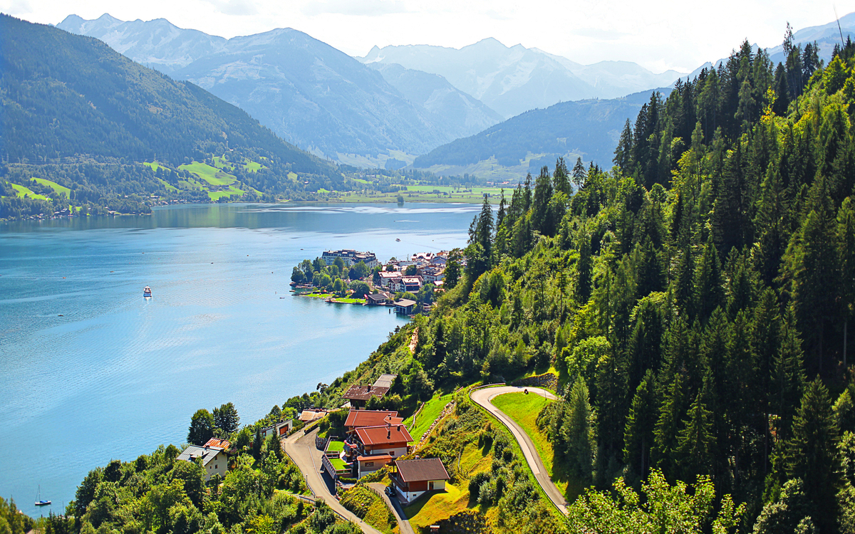 Blick auf einen See in den Alpen, umgeben von Wäldern und Bergen.