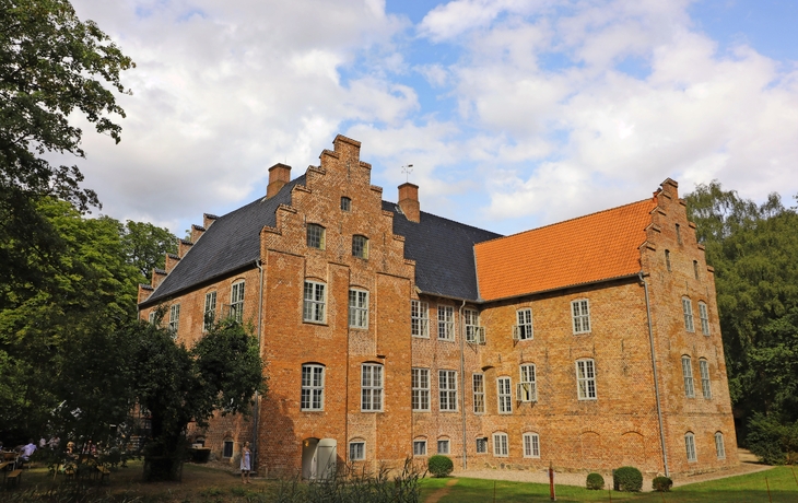 Reetdachhaus mit weißem Zaun und Garten im Hintergrund.