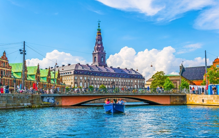 Menschen in einem blauen Boot auf einem Kanal vor historischem Gebäude an einem sonnigen Tag.