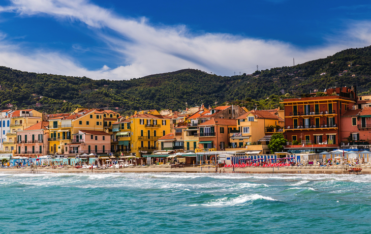 Bunte Häuser und Strand vor grünen Hügeln an der Küste