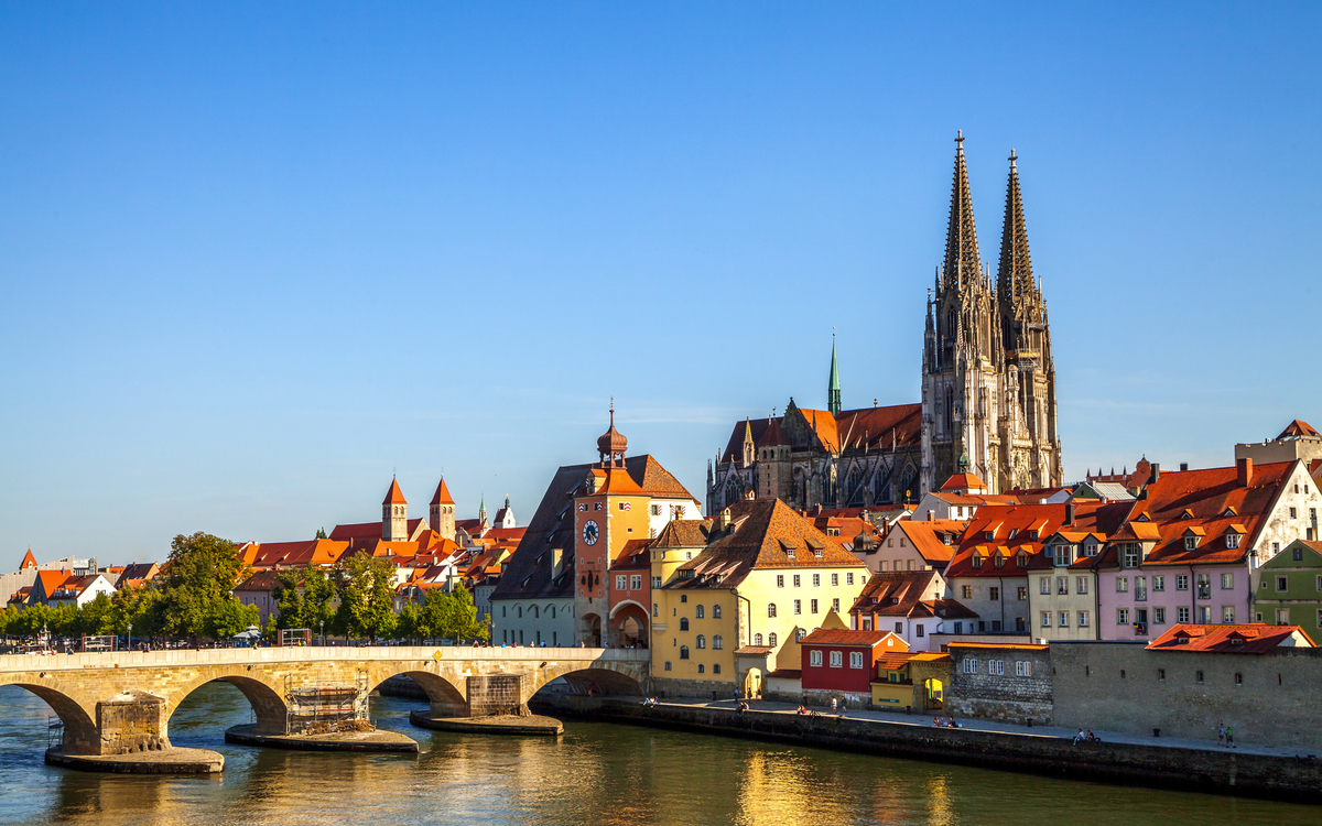 Stadtansicht mit Brücke und Kathedrale an einem Fluss bei Sonnenschein.