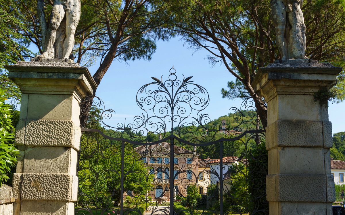 Eingangstor zu einer historischen Villa in Abano Terme, umgeben von Bäumen und zwei Statuen.