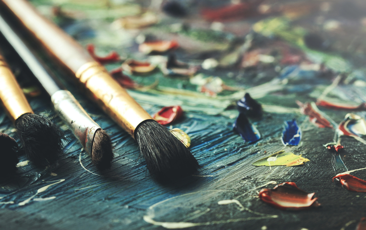 Pinsel liegen auf einer Leinwand mit verschiedenen Farbflecken und Farbtupfern.